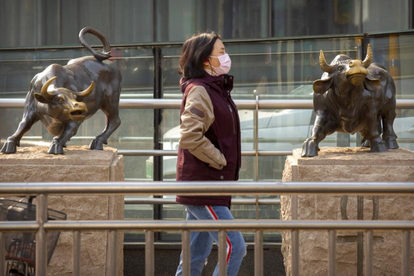 Seorang warga berjalan di depan patung saham di Beijing, Jumat (28/2). 