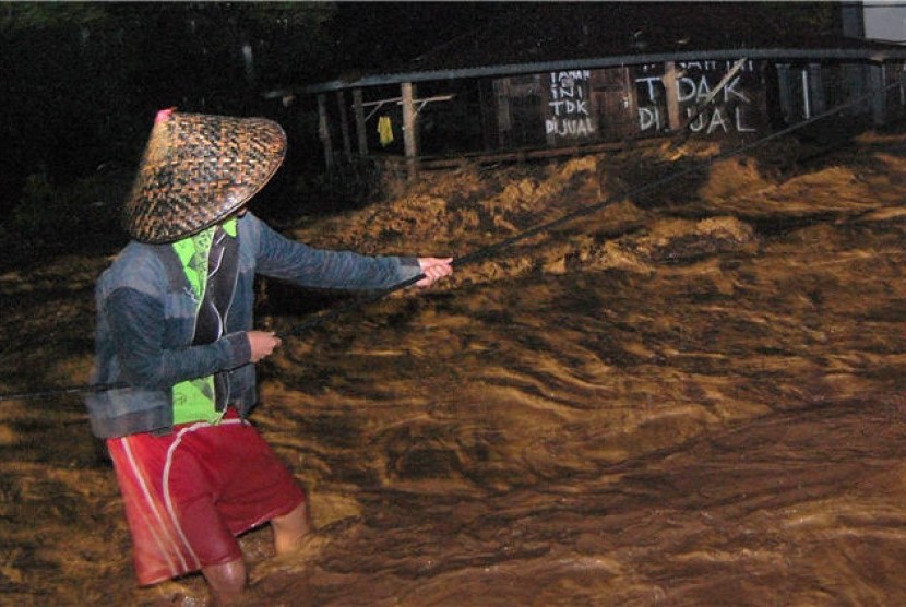  Seorang warga berpegangan pada sebuah tali melintasi banjir di Kelurahan Limaumanis, Kecamatan Pauh, Padang, Sumbar, Selasa (24/7) malam. 
