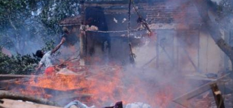 Seorang warga melemparkan batu ke arah bangunan rumah, musholla dan madrasah yang dibakar massa, di Desa Blu'uran, Karangpinang, Sampang, Madura, Jatim, Kamis (29/12). 