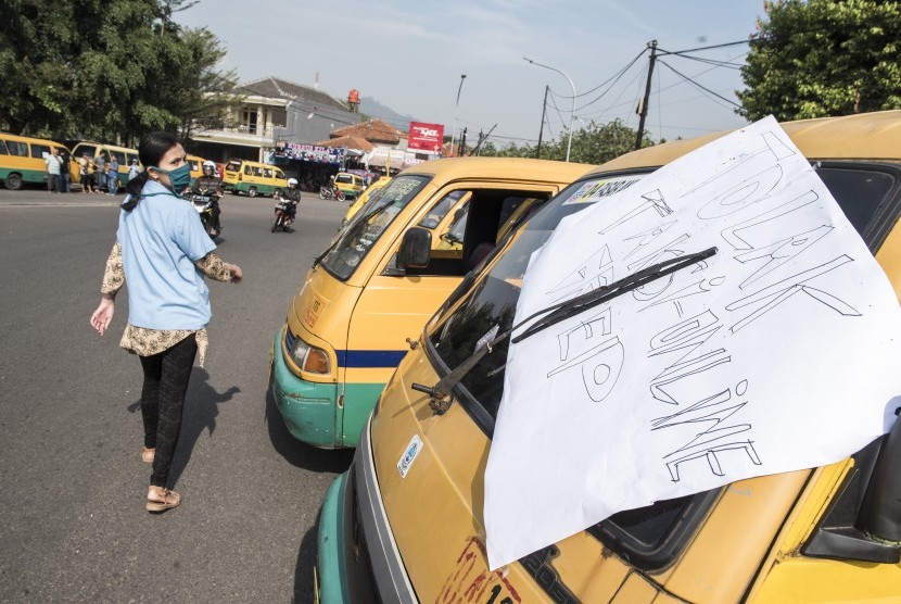 Seorang warga melintas di depan angkutan umum saat unjuk rasa sopir angkutan umum dari empat trayek di Bundaran Leuwigajah, Cimahi Selatan, Kota Cimahi, Jawa Barat, Senin (25/9). 
