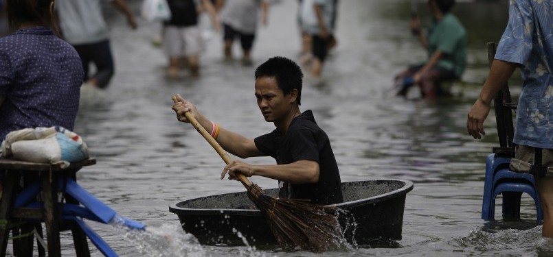 Seorang warga melintasi jalan di kota Bangkok dengan menggunakan wadah serta sapu sebagai dayung, Jumat, 28/10. (AP)