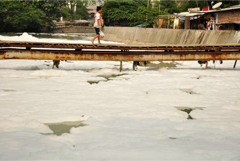 Seorang warga melintasi jembatan kayu di atas sungai yang tercemar. (ilustrasi) 