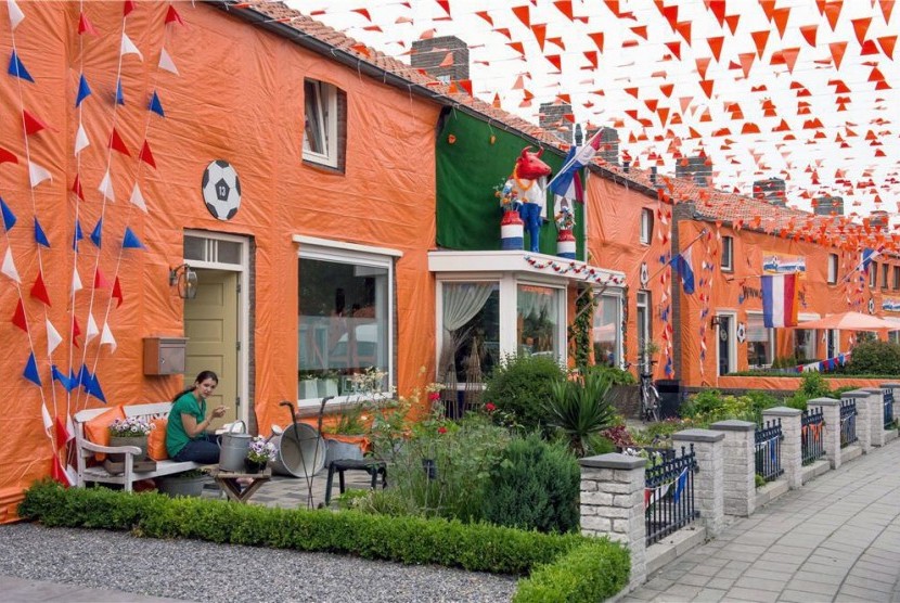 Seorang warga membaca buku di depan rumahnya di Goirle, Belanda, yang dihiasi dengan bendera, atribut, dan warna khas timnas Belanda. Belanda Umumkan Kembali Adopsi Anak dari Negara Lain