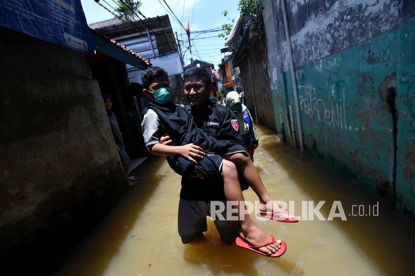 Seorang warga membawa anaknya yang baru selesai dikhitan melewati banjir di kawasan permukiman di Petogogan, Kebayoran Baru, Jakarta Selatan, Senin (5/10/2020). Banjir tersebut terjadi akibat meluapnya Kali Krukut. 