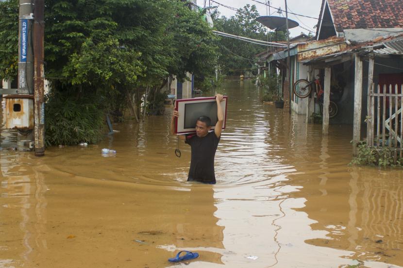 Seorang warga membawa televisi melintasi banjir di Desa Dawuan Tengah, Cikampek, Karawang, Jawa Barat, Jumat (19/2/2021). Banjir yang kembali melanda wilayah itu disebabkan tingginya intensitas hujan dan mengakibatkan meluapnya air Sungai Cikaranggelam yang merendam ratusan rumah warga.