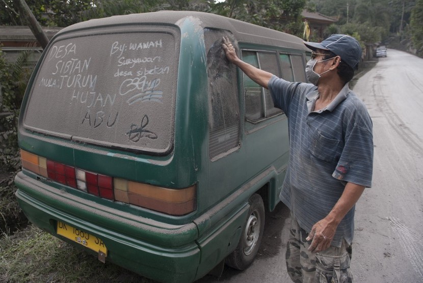 Seorang warga membersihkan mobilnya dari abu letusan Gunung Agung, di Desa Sebetan, Karangasem, Bali, Ahad (26/11).