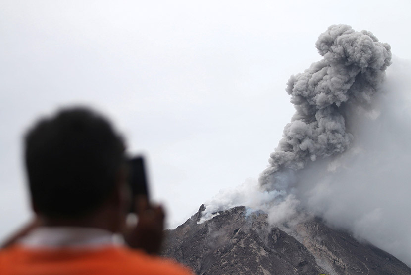 Seorang warga memotret Gunung Sinabung mengeluarkan material vulkanis ketika erupsi, tampak dari Desa Tiga Serangkai, Karo, Sumatera Utara, Jumat (13/11).