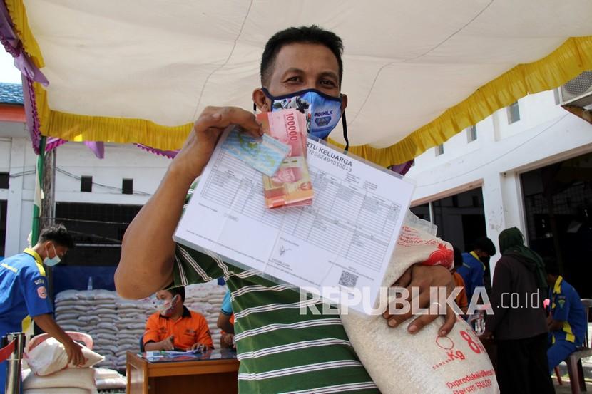 Seorang warga memperlihat sejumlah uang dan beras bantuan sosial (bansos) dari pemerintah pusat (ilustrasi)