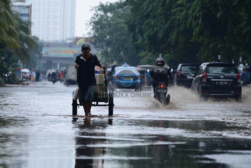 Seorang warga mendorong gerobak untuk melintasi genangan air yang mulai surut di Kawasan Kelapa Gading, Jakarta Utara, Jumat (13/2).    (Republika/Raisan Al Farisi)
