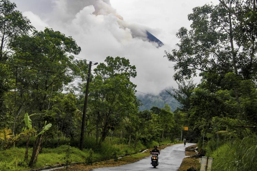 Seorang warga mengendarai sepeda motor melewati jalan saat Gunung Merapi memuntahkan material vulkanik di latar belakang, terlihat dari desa Cangkringan di Sleman, Yogyakarta, Kamis, 10 Maret 2022.