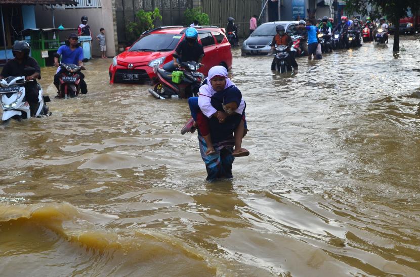 Seorang warga menggendong anaknya saat melintasi jalan yang terendam banjir di Kudus, Jawa Tengah (ilustrasi) 