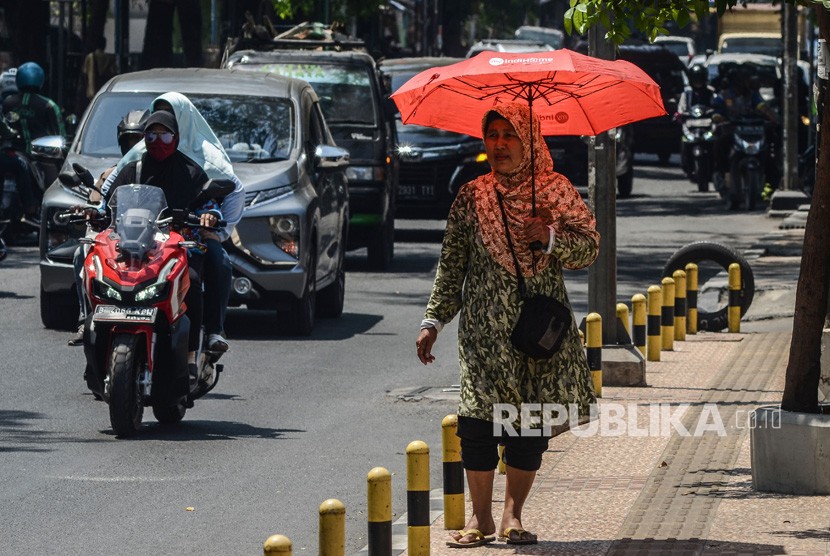 Seorang warga menggunakan payung saat cuaca terik di jalur pedestrian Jalan Juanda, Kota Bekasi, Jawa Barat, Selasa (22/10/2019).