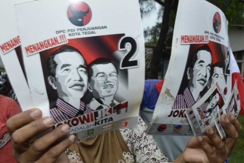 Seorang warga menunjukkan poster bergambar Joko Widodo - Jusuf Kalla di kawasan Pelabuhan Perikanan Pantai Tegalsari, Tegal, Jawa Tengah, Kamis (19/6). 