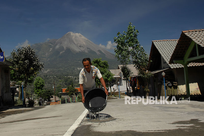 Seorang warga menyiram jalan raya yang tertutup abu vulkanis Gunung Merapi di Wonolelo, Sawangan, Magelang, Jawa Tengah, Jumat (1/6).