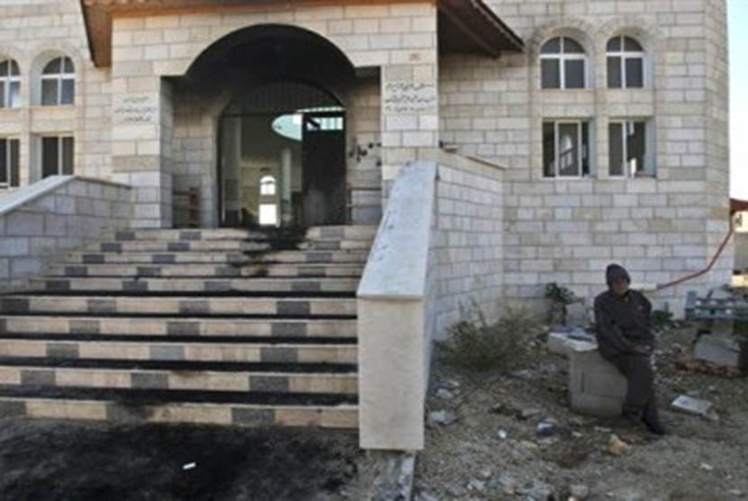 Seorang warga Palestina duduk di luar masjid yang dibakar warga Yahudi di Tepi Barat, Nablus, Rabu (7/12). 