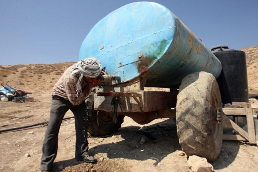 Seorang warga Palestina  yang tinggal di Area C, Tepi Barat, meminum air langsung dari tangki penyimpanan air. Israel membatasi bahkan meniadakan akses ke sumber-sumber alam untuk warga Palestina di kawasan tersebut (Ilustrasi)