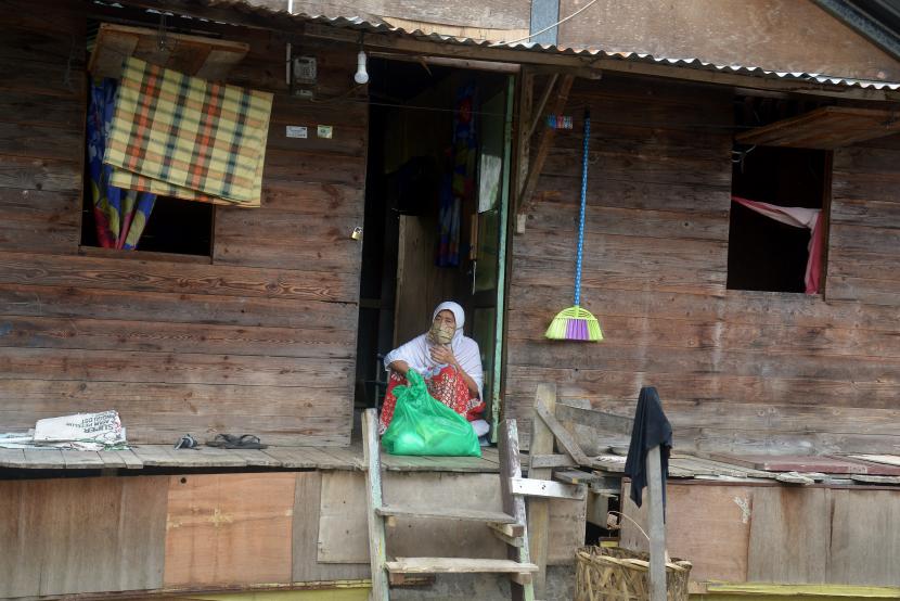 Seorang warga prasejahtera duduk di teras rumahnya memegang kantong pasltik berisi kebutuhan pokok seusai diserahkan langsung oleh personil Polri dan TNI di Kelurahan Kampung Mulia, Kecamatan Kuta Alam, Banda Aceh, Aceh, Jumat (10/4/2020). Menurut data pemerintah Aceh sebanyak 61.584 kepala keluarga (KK) yang ekonominya terdampak pandemi COVID-19 di daerah itu mendapatkan bantuan bahan pokok dan uang tunai.