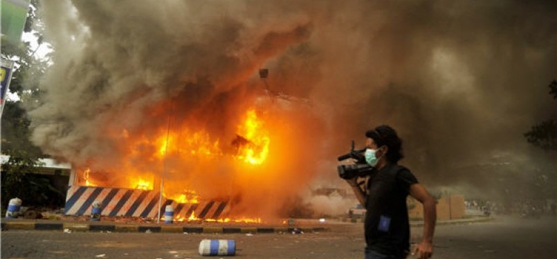 Seorang wartawan melintas di dekat pos polisi yang dibakar demonstran saat aksi unjuk rasa menolak kenaikan harga bahan bakar minyak (BBM).  (ilustrasi)