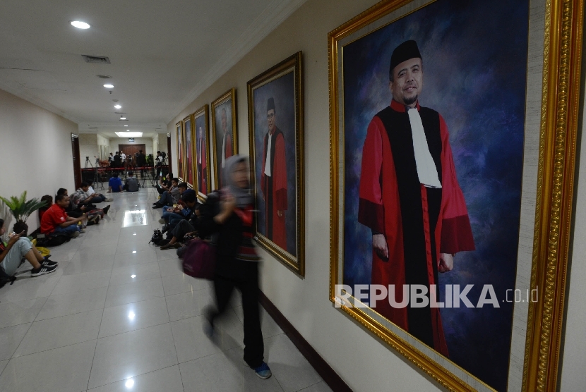 Seorang wartawan melintasi lukisan Hakim Mahlamah Konstitusi Non Aktif Patrialis akbar saat berlangsungnya rapat antara Komisi III DPR Bersama Hakim Mahkamah Konstitusi (MK) di Gedung Mahkamah Konstitusi, Jakarta, Senin (30/1).