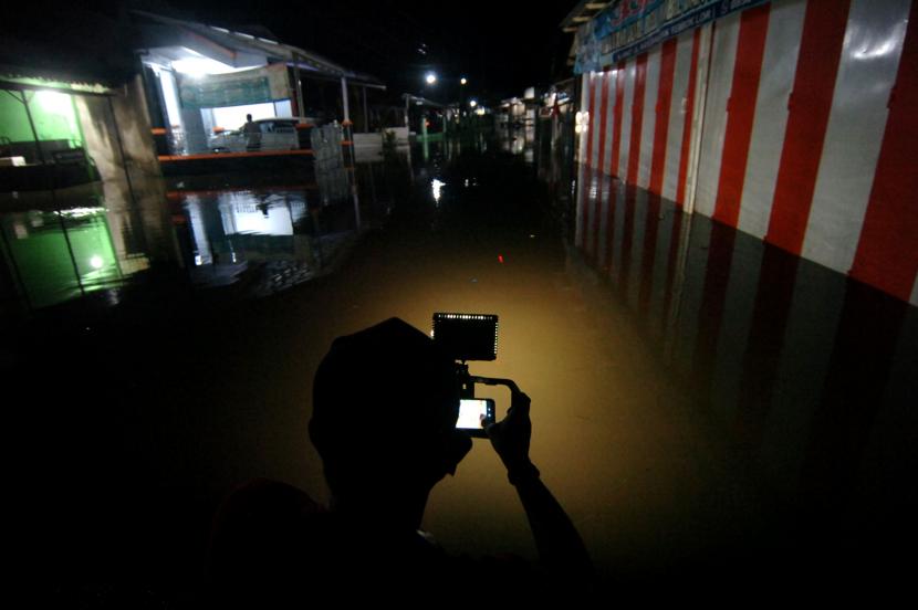Seorang wartawan mengambil gambar rumah yang tergenang banjir. Ilustrasi