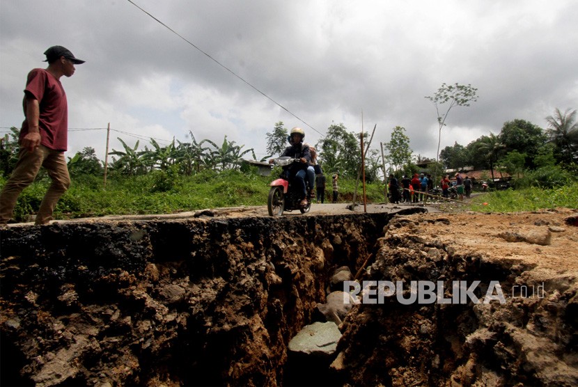 Sepeda motor melintas di jalan yang terbelah akibat pergerakan tanah di jalur wisata, Karang Tengah, Sentul, Kabupaten Bogor.