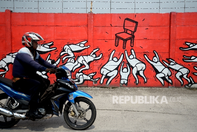 Sepeda motor melintas di sekitar mural yang mengambarkan tentang kursi kekuasaan di Jakarta, Jumat (24/3).