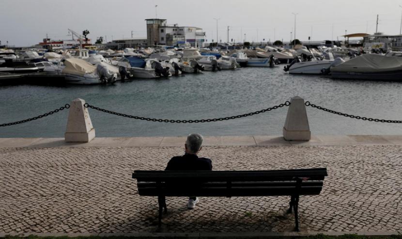 Seseorang duduk di sebuah pantai di Portugal yang sepi karena pandemi.