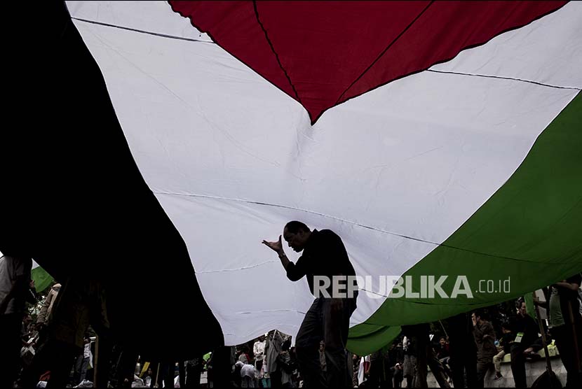 Siluet massa aksi melintas di dalam bendera Palestina raksasa saat aksi unjuk rasa di depan Kedutaan Besar Amerika Serikat, Jakarta, Jumat (23/6). Aksi tersebut dalam rangka peringatan International al-Quds Day dan memberikan dukungan bagi rakyat Palestina serta mengecam kebujakan-kebijakan Amerika Serikat dan Israel. 