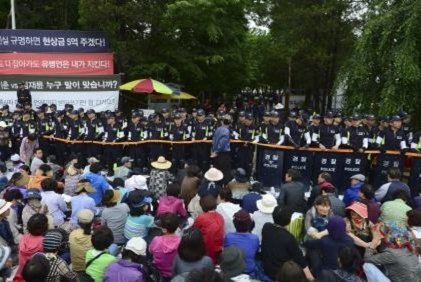 South Korean policemen stand guard in front of the main gate of the Evangelical Baptist Church premises, as church believers sit in front of the police barricade, in Anseong June 11, 2014.