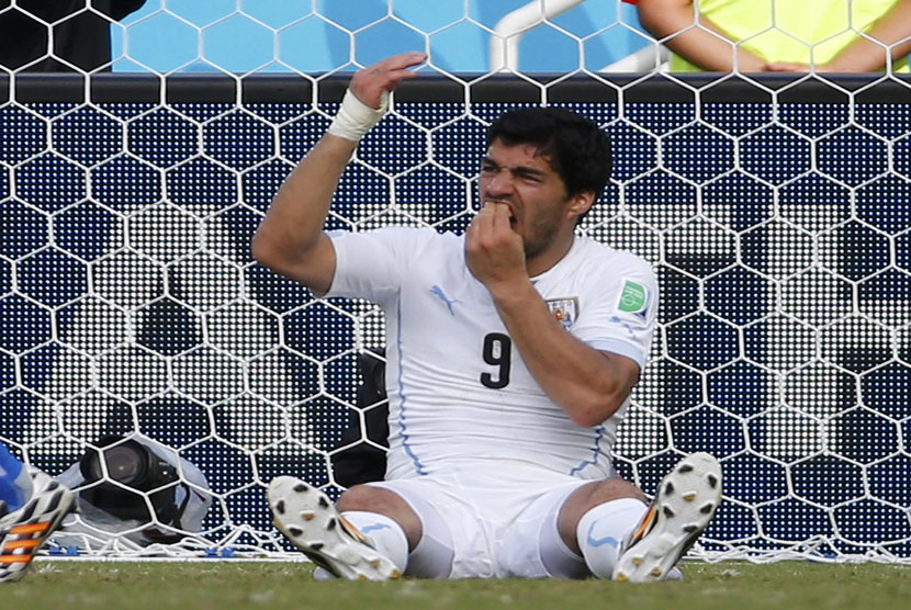 Striker Timnas Uruguay, Luis Suarez, memegangi giginya usai terlihat menggigit pemain Italia, Giorgio Chiellini, di laga terakhir Grup D Piala Dunia 2014 Brasil di Arena Dunas, Natal, Selasa (24/6).