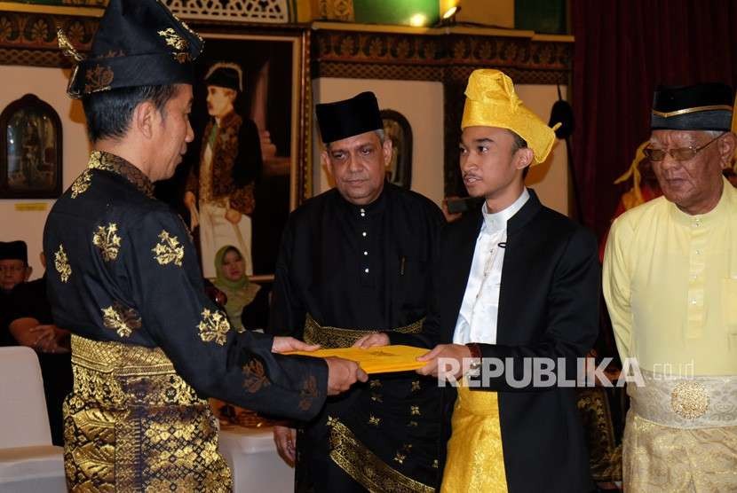 Sultan Deli Ke-XIV Tuanku Mahmud Arya Lamanjiji Perkasa Alam (kedua kanan) menyerahkan berkas kepada Presiden Joko Widodo (kiri) pada prosesi pemberian gelar adat Melayu Deli, di Istana Maimun, Medan, Sumatera Utara, Ahad (7/10).