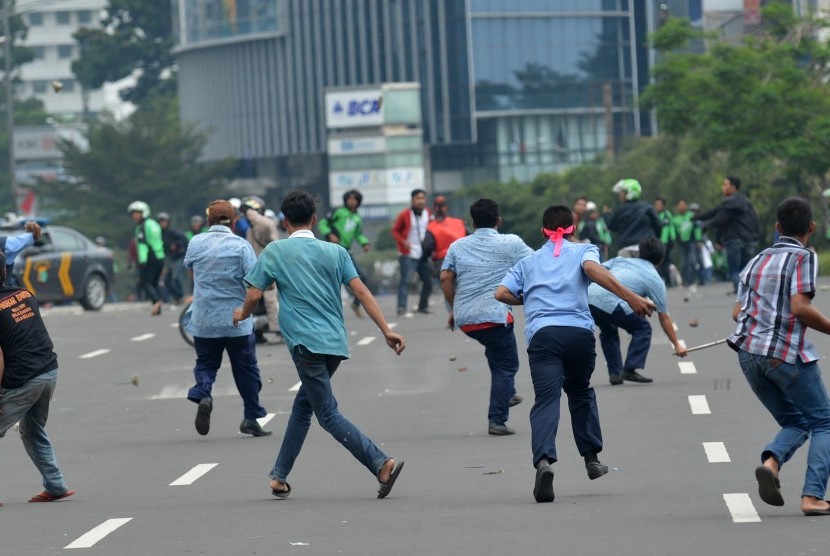 Sopir taksi dan pengemudi ojek berbasis aplikasi saling lempar batu saat aksi menolak keberadaan angkutan umum online di Jakarta, Selasa (22/3).
