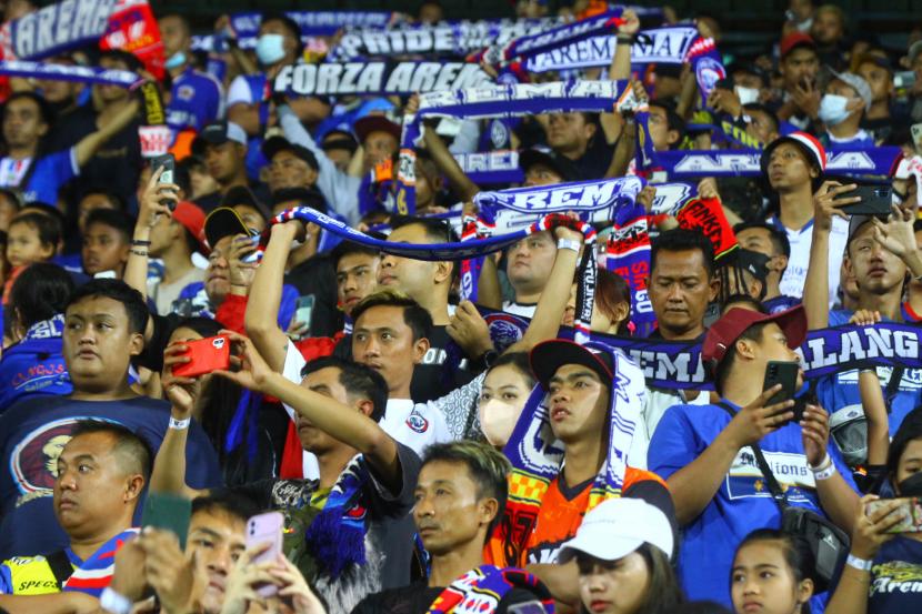 Suporter kesebelasan Arema FC atau Aremania mengangkat syal untuk memberi semangat kepada tim kesayangannya saat bertanding melawan PSIS Semarang dalam pertandingan persahabatan di Stadion Kanjuruhan, Malang, Jawa Timur, Ahad (22/5/2022). Arema akan kembali beruji coba di Stadion Kanjuruhan pada Selasa (7/6/2022) melawan Rans Nusantara FC.