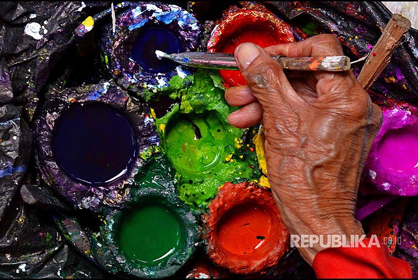 Tangan perajin mecelupkan cat untuk melukis pada payung