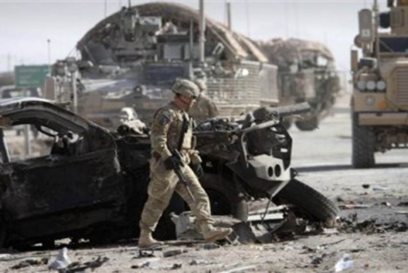 Tentara Amerika Serikat yang tergabung dalam Pasukan Bantuan Keamanan Internasional (ISAF) pimpinan NATO berjalan melewati bangkai kendaraan.