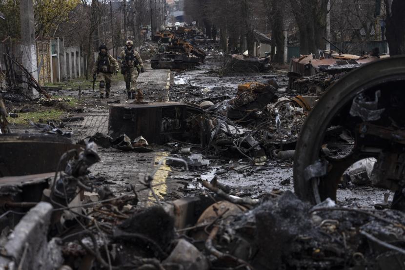 Tentara berjalan di tengah tank Rusia yang hancur di Bucha, di pinggiran Kyiv, Ukraina, Minggu, 3 April 2022. Pasukan Ukraina menemukan mayat-mayat brutal dan kehancuran yang meluas di pinggiran kota Kyiv, memicu seruan baru untuk penyelidikan kejahatan perang dan sanksi terhadap Rusia. 