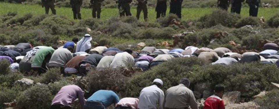 Tentara Israel berjaga-jaga di depan demonstran Palestina yang sedang sholat.