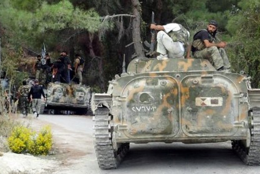 Tentara Pembebasan Suriah (FSA) berpose di atas tank yang berhasil mereka rebut dari militer Suriah di sebuah desa di Provinsi Idlib, Suriah.