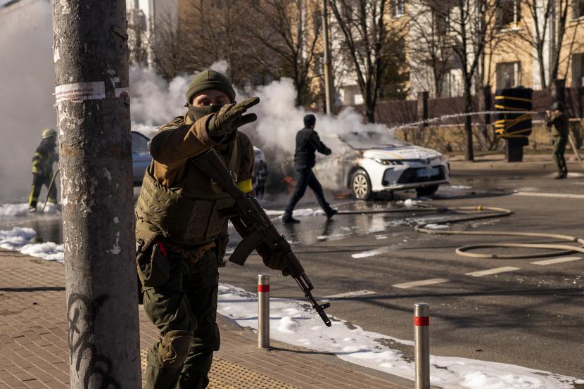 Tentara Ukraina mengambil posisi di luar fasilitas militer saat dua mobil terbakar, di sebuah jalan di Kyiv, Ukraina, Sabtu, 26 Februari 2022. Pasukan Rusia menyerbu ke arah ibu kota Ukraina Sabtu, dan pertempuran jalanan pecah saat pejabat kota mendesak penduduk untuk berlindung .
