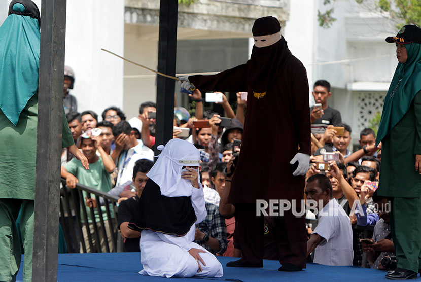 Terpidana (duduk) pelanggar peraturan daerah (qanun) tentang syariat islam menjalani eksekusi hukuman cambuk di hadapan warga di halaman Masjid Jami' Kemukiman Lueng Bata, Banda Aceh, Aceh, Jumat (20/4). 