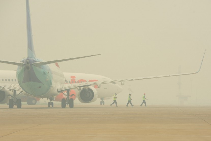 Tiga kru bandara melewati dua pesawat di landasan Bandara Supadio yang diselimuti kabut asap, di landasan Bandara Supadio, Kubu Raya, Kalbar, Rabu (21/10). 