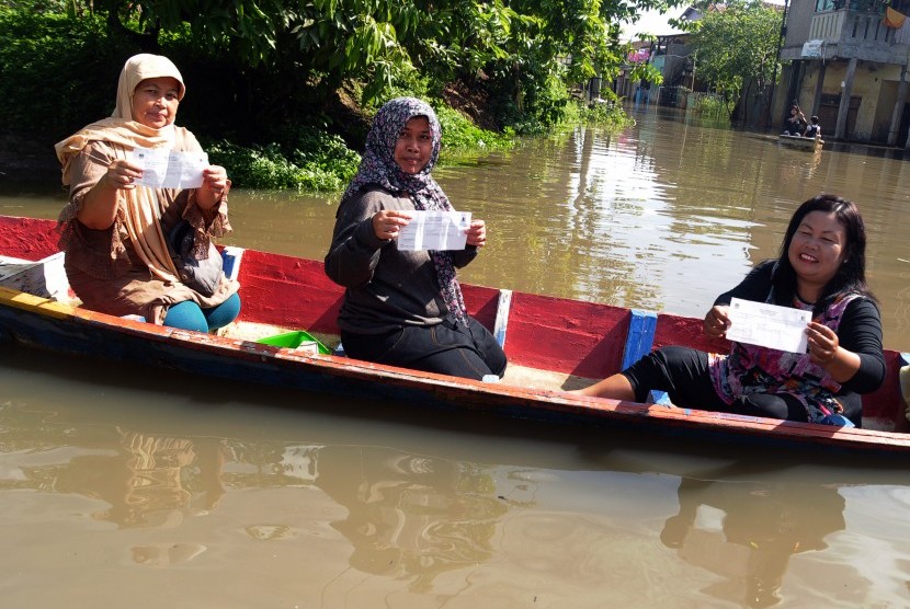 Tiga orang warga menunjukkan formulir hak pilih Pilkada Kabupaten Bandung saat akan menuju TPS dengan menggunakan perahu karena banjir di Kampung Cieunteung, Baleendah, Kabupaten Bandung, Jawa Barat, Rabu (9/12). 