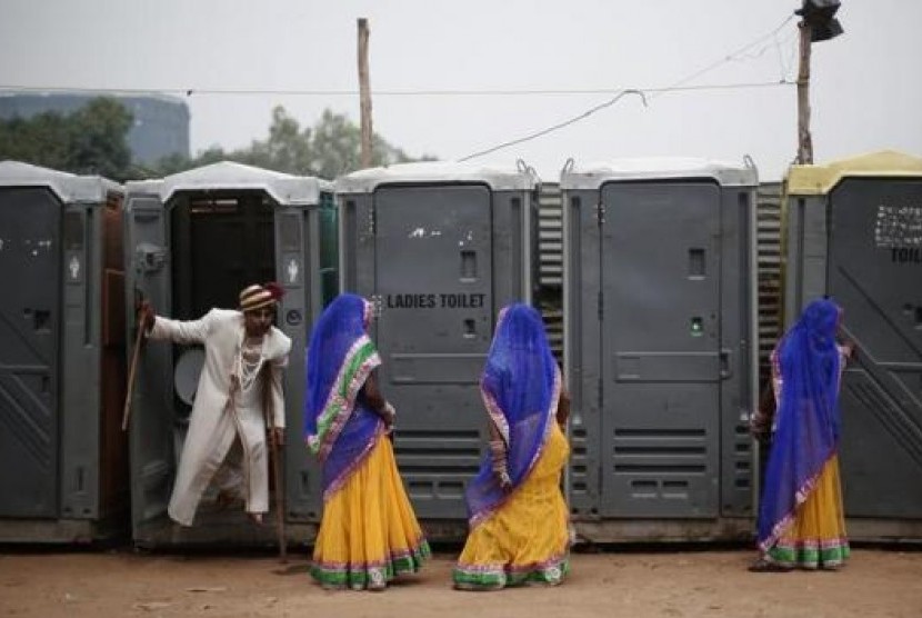 Tiga perempuan India mengantre di toilet umum.
