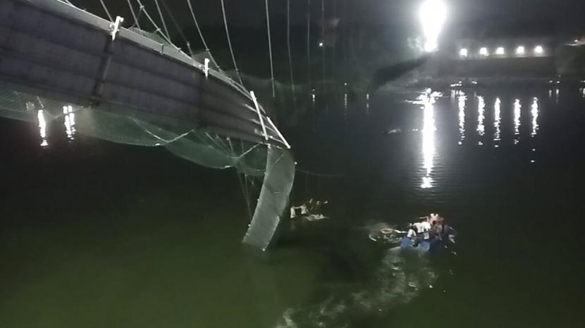 Tim penyelamat di kapal mencari di Sungai Machchu di sebelah jembatan kabel yang runtuh di distrik Morbi, negara bagian Gujarat, India, Ahad, 30 Oktober 2022. Puluhan dikhawatirkan tewas dan beberapa terluka dalam kecelakaan jembatan roboh itu. 
