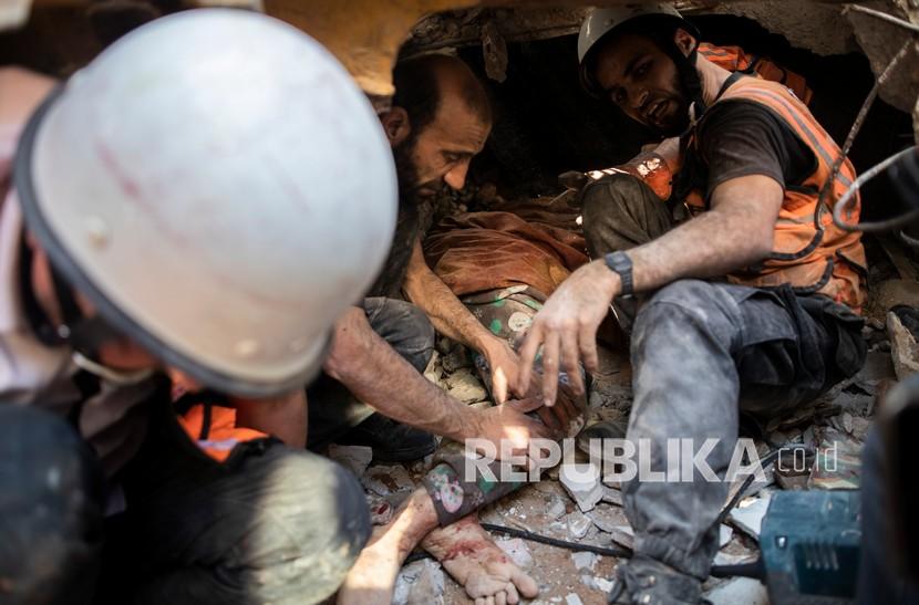 Tim penyelamat Palestina menarik tubuh seorang wanita dari bawah reruntuhan bangunan tempat tinggal yang hancur menyusul serangan udara mematikan Israel di Kota Gaza yang meratakan tiga bangunan dan menewaskan sedikitnya 26 orang, di Kota Gaza, Ahad (16/5).