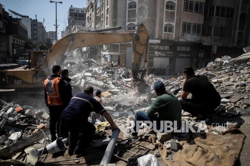  Tim penyelamat Palestina mencari korban di bawah reruntuhan bangunan tempat tinggal yang hancur setelah serangan udara Israel yang mematikan di Kota Gaza, Ahad (16/5).
