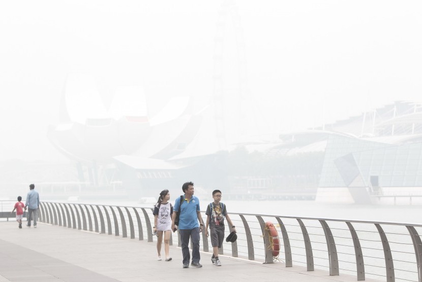 Turis berjalan di area Marina Bay Sands, Singapura, yang tertutup kabut asap akibat kebakaran hutan di Indonesia (23/10).