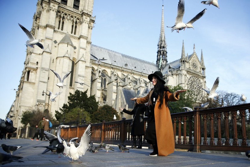 Turis berpose dengan latar Notre Dame de Paris.