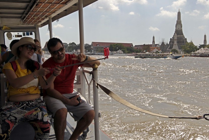 Turis berpose dengan latar Wat Arun di Bangkok.