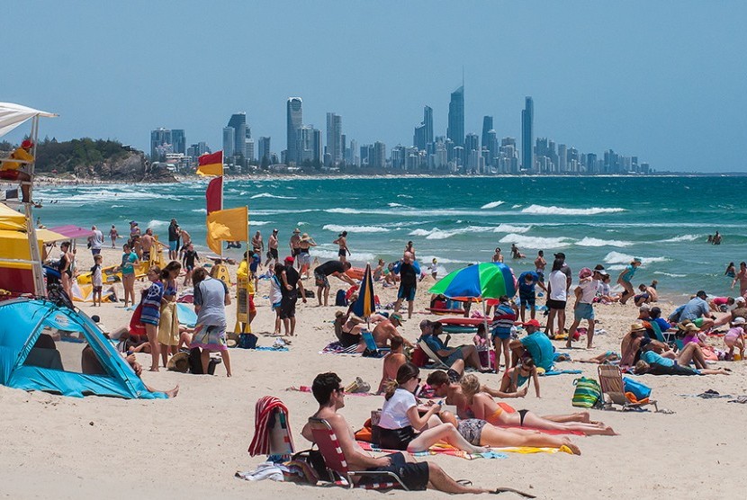 Turis bersantai di pantai berpasir putih dengan pemandangan bangunan pencakar langit Gold Coast, Australia.